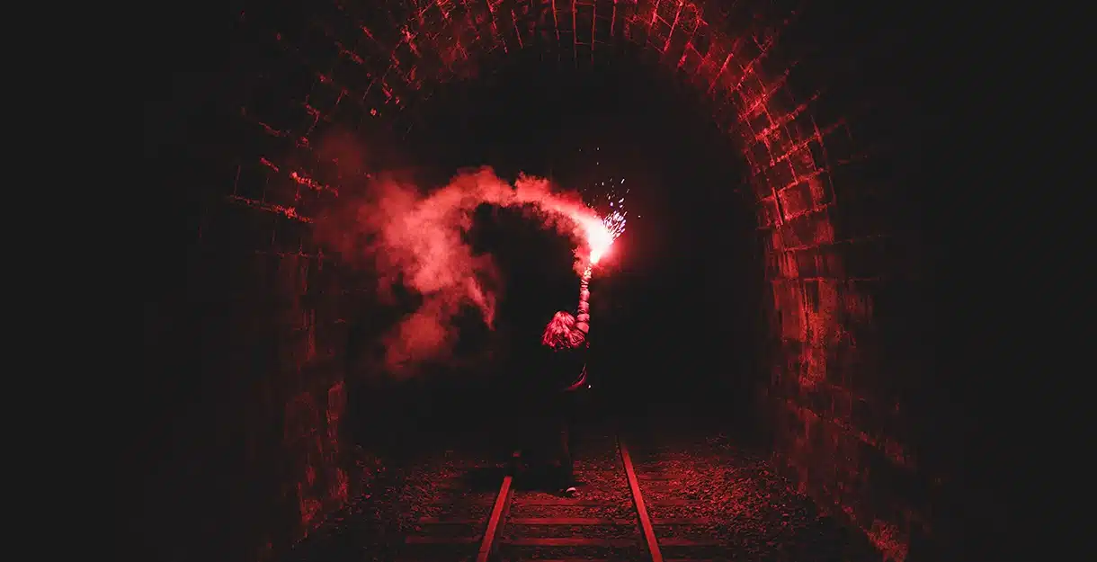 A woman holding a bright red flare inside a dark railroad tunnel.
