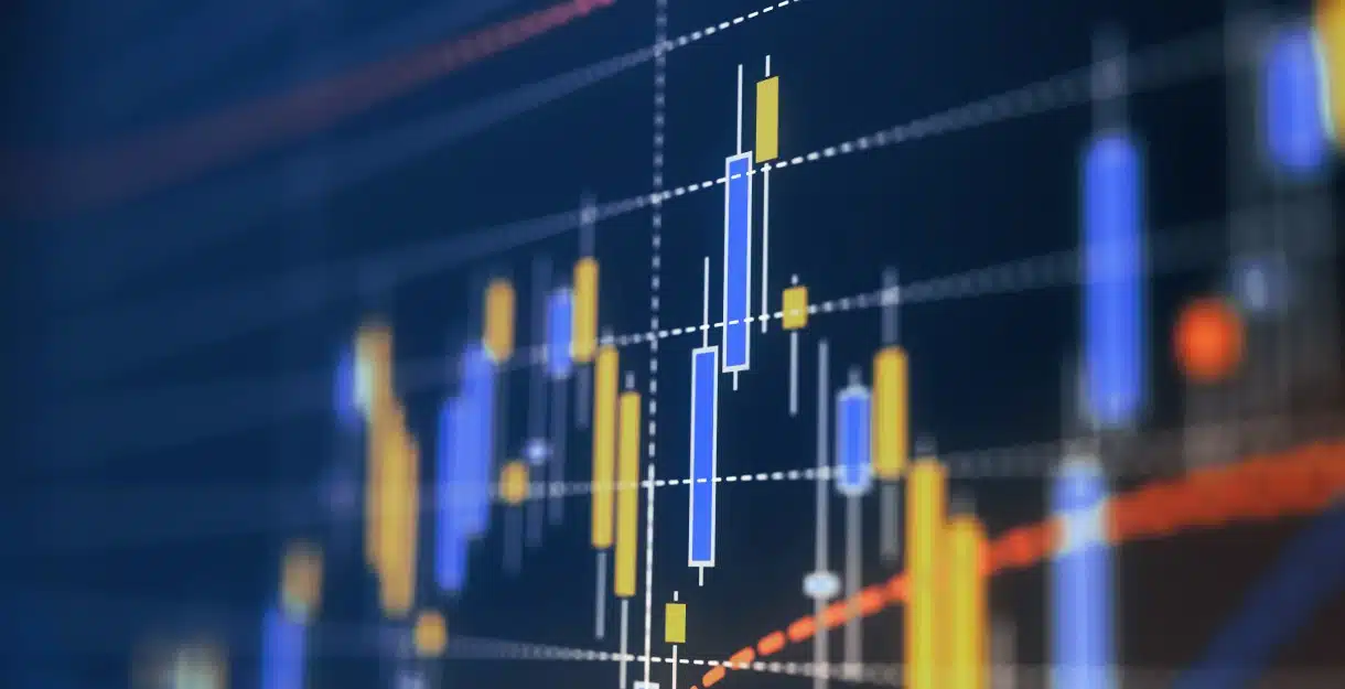 A close-up, digital stock market candlestick chart showing price fluctuations in blue and yellow against a dark blue background.