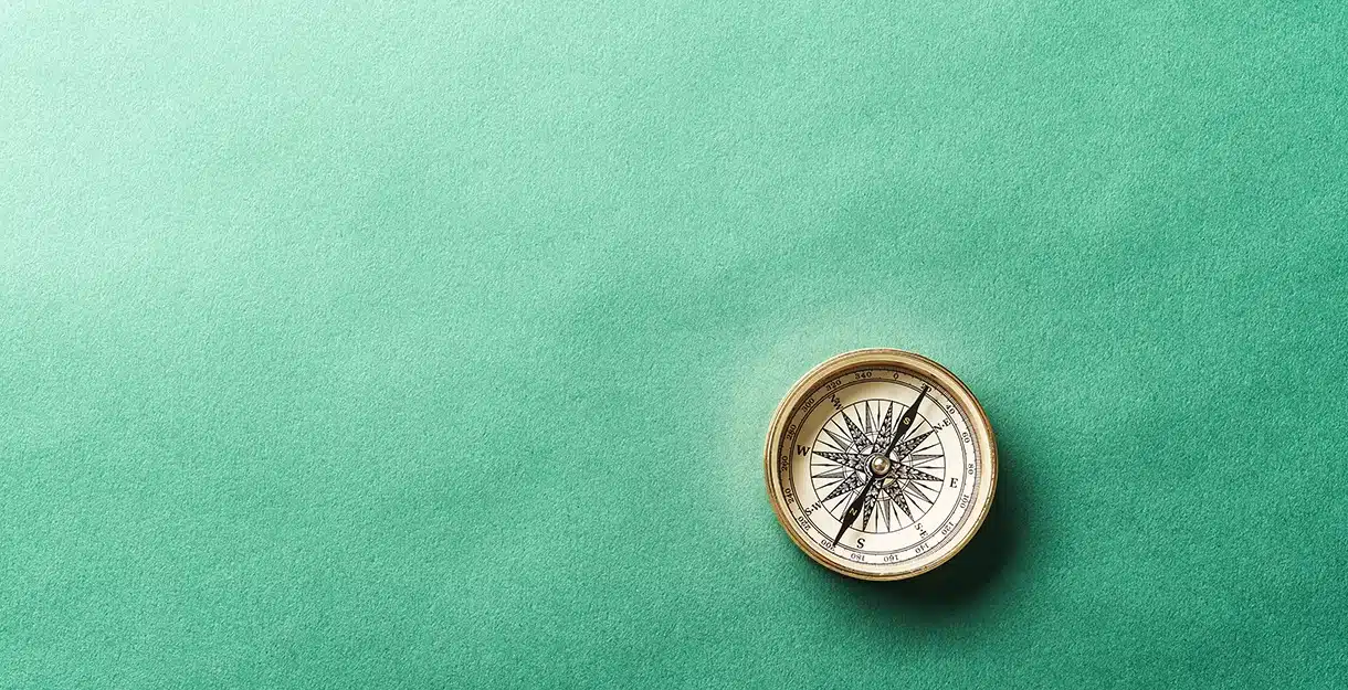A vintage brass compass on a textured green background.