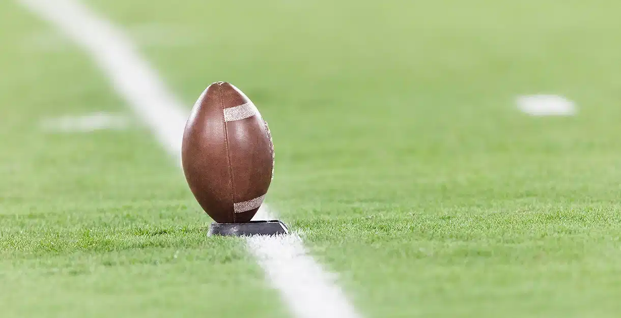 An American football on a tee on a green field.