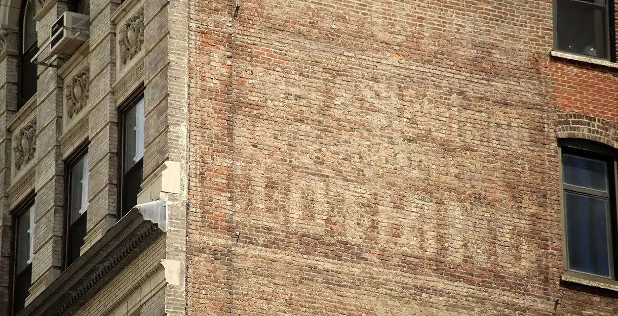 A close-up of a vintage, faded advertisement painted directly onto the side of an old red brick building.