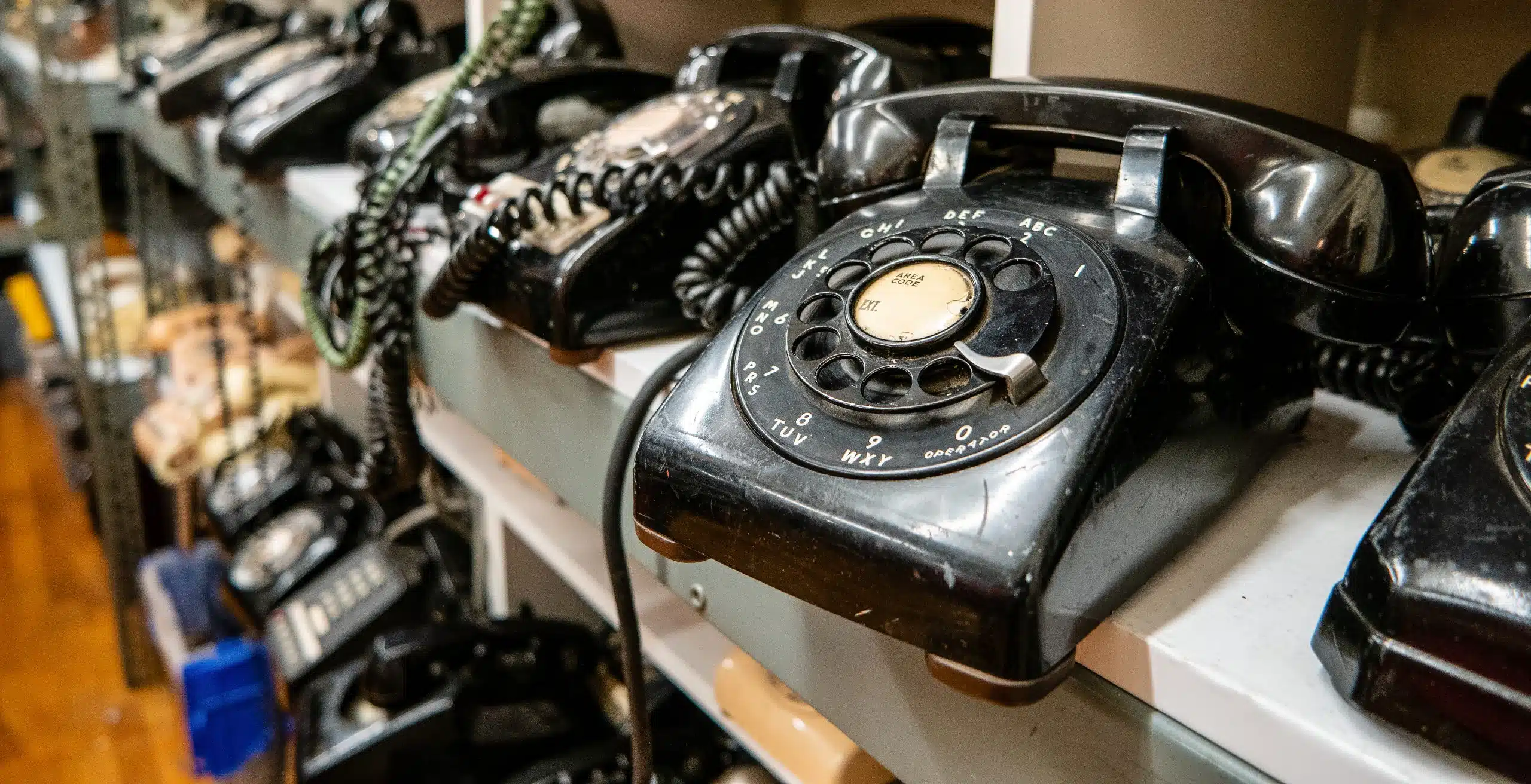 A close-up view of several rows of old-fashioned black rotary dial telephones sitting on storage shelves.